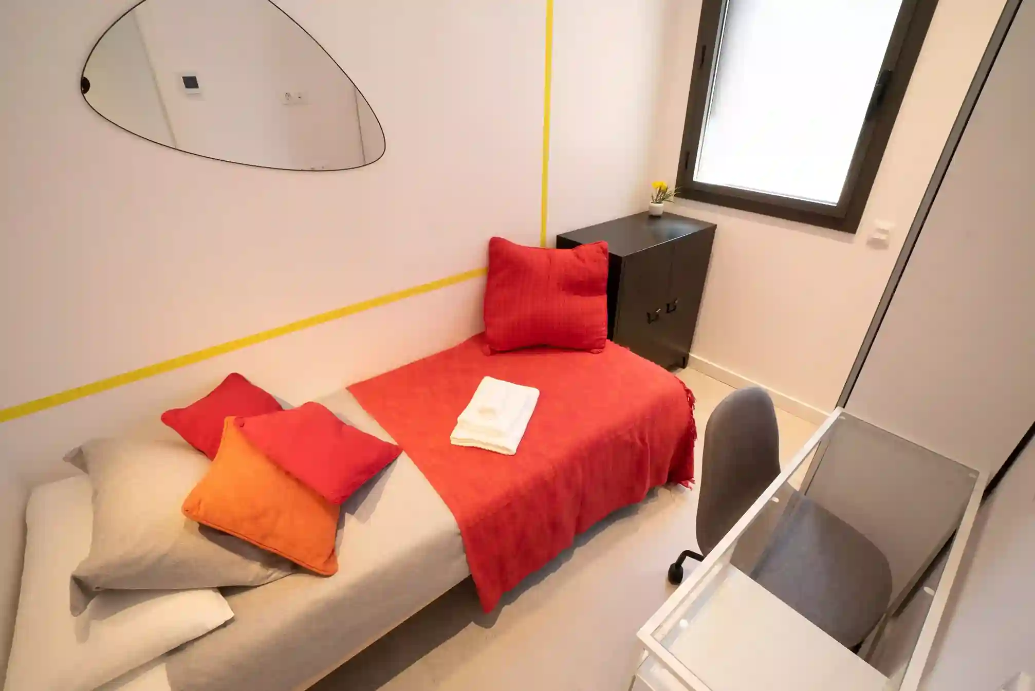 Habitación Badal individual en Coliving Vibes Rosselló, con cama individual, escritorio y decoración en tonos rojos y naranjas